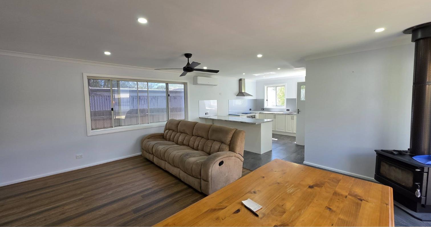 Open-plan living and kitchen after painting, with a lounge and dining table in front of a white kitchen