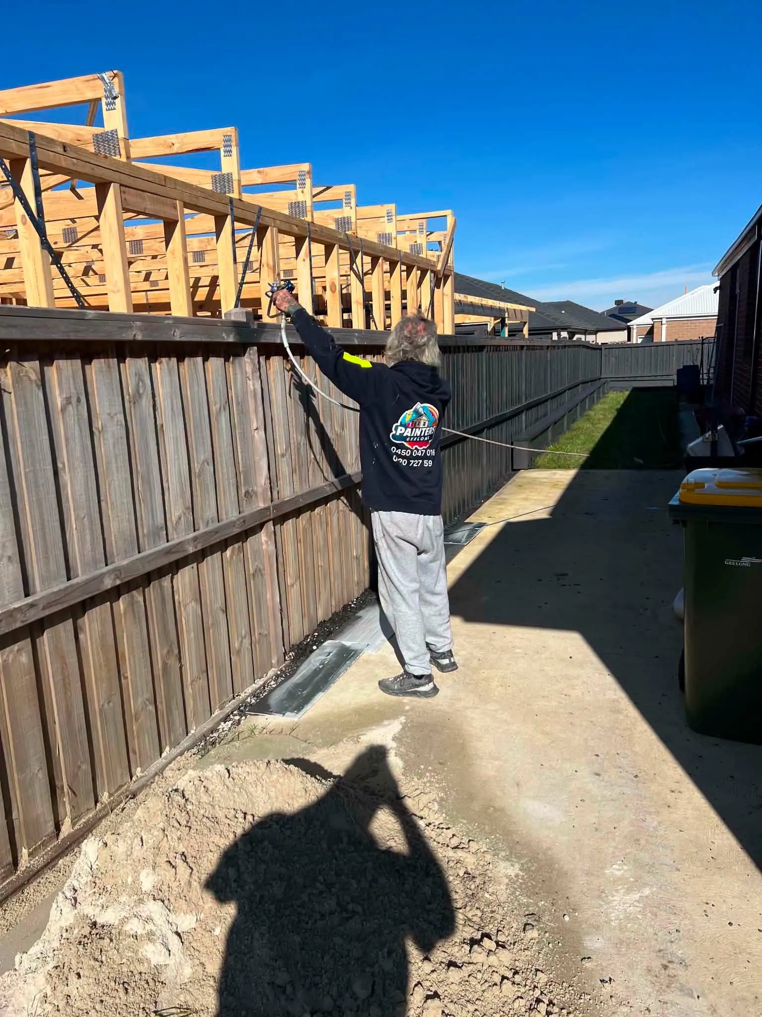 Painter working beside a timber fence under a clear blue sky