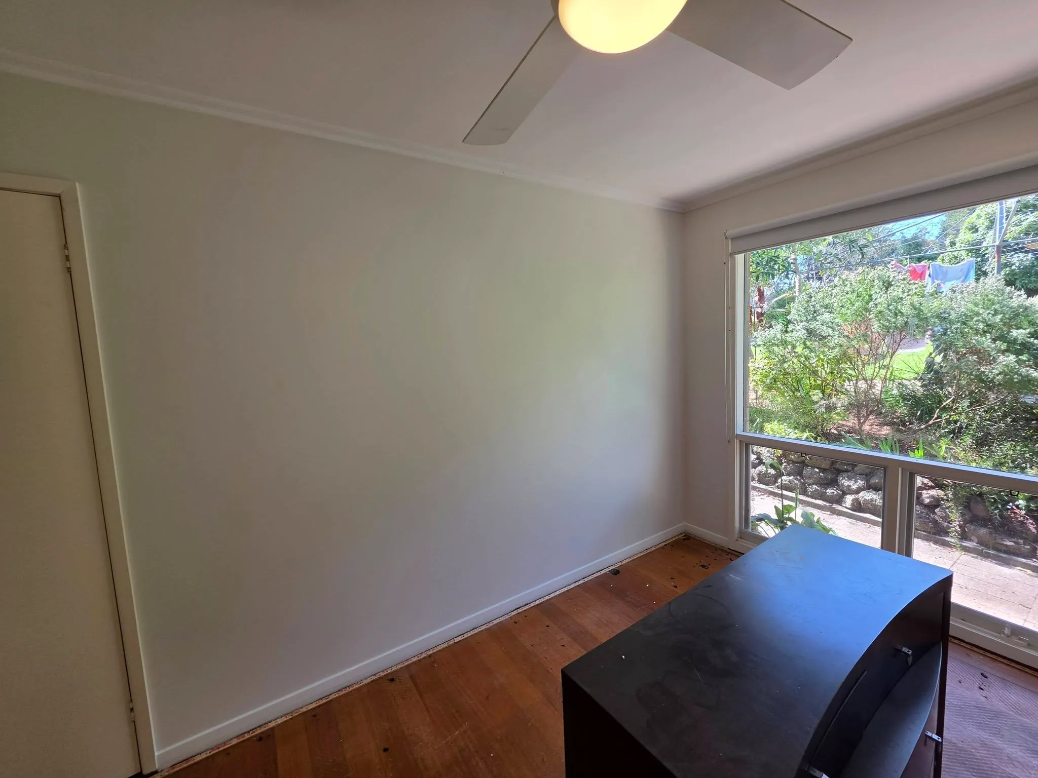 Freshly painted bedroom with white walls, ceiling fan and garden view
